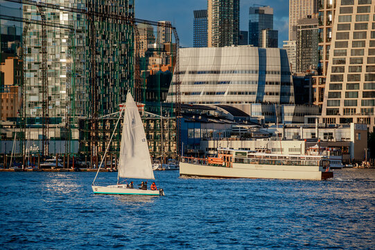 Modern Chelsea waterfront with IAC Building in New York City. Sailing boat and ferry pass the glass architecture of Frank Gehry design along the Manhattan riverbank.