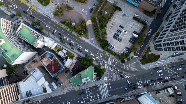 Aerial view of a busy urban intersection with multi-lane roads, crosswalks, parked cars in a lot, and surrounding modern buildings with green rooftops in Busan, Busan, South Korea.
