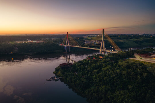 Aerial view of the Integration Bridge spanning the river at sunset, with lush forest surroundings and golden light reflecting on the water in Foz do Iguacu, State of Parana, Brazil.