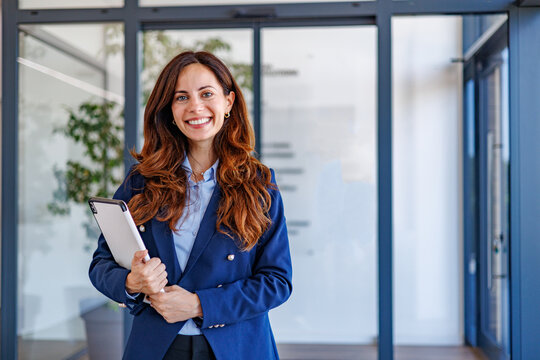 Confident businesswoman smiling, holding digital tablet in modern office, portraying professional success and leadership