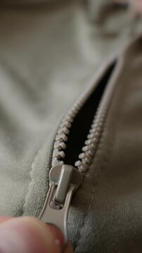 A close-up view of a hand pulling the slider of a zipper on an olive green jacket. Concept of getting dressed, preparing for cold weather, and everyday casual fashion.