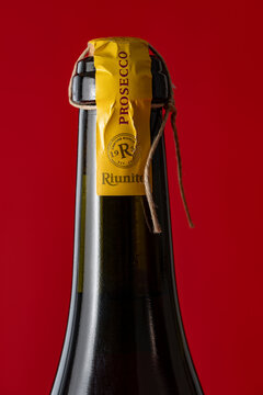 Italian Riunite Prosecco sparkling wine bottle with yellow seal and twine string on red background. Minimalist photography for alcohol branding, holiday ads and bar menus