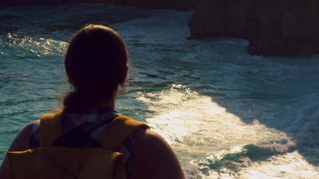 Female Traveler Watching Powerful Ocean Waves From Cliff Edge During Golden Hour Coastal Adventure in Slow Motion