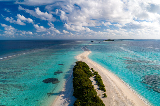Aerial view of Dhigurah Island sandbar and green spit in South Ari Atoll, Maldives. Turquoise lagoon shows reefs and coral, gentle surf, midday light, cumulus clouds.