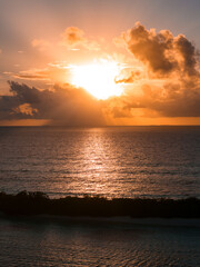 Fototapeta premium Sun breaks through towering cumulus clouds near Dhigurah Island, Maldives, casting a golden path on calm water, with a thin island silhouette and soft reflections.