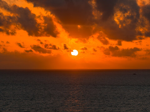 Sun sets over the open sea near Dhigurah island, Maldives. A tiny boat dots the water as clouds glow at their edges. Long focal length and balanced exposure guide the view.