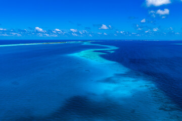 Fototapeta premium Aerial view shows Dhigurah Island reef in South Ari Atoll, Maldives. Turquoise shallows curve through deep ocean, sandbars and coral shelves appear under clear water.