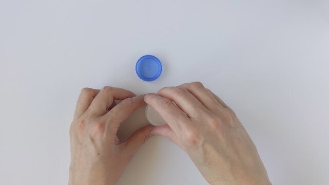 Hands tighten the lid of a contact lens case. Concept for eye care and lens hygiene. White and blue container with compartments for safe contact lens storage.
