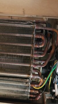 Exposed dirty copper freon tubes and dusty fins inside a disassembled wall air conditioner. Concept of indoor air quality hazards, dangerous mold growth, and professional maintenance.