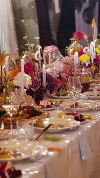 Vertical video. Wedding banquet table with flowers, candles, plates and glasses prepared for guests outdoors.