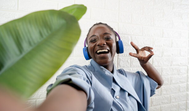Joyful young woman laughing and gesturing while taking a selfie near a green plant