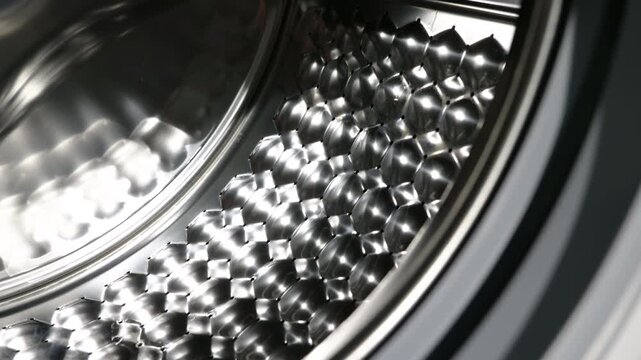 Washing machine drum closing with automatic door. Detailed close-up shot of an empty washing machine's shiny stainless steel drum with a modern hexagonal pattern as the automatic door slowly closes