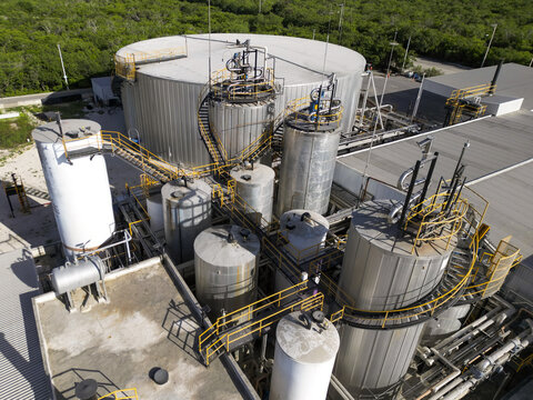 Aerial view of the Ergon Asfaltos Progreso industrial facility with large metal storage tanks, complex piping, and elevated walkways surrounded by greenery in Progreso, Yucatan, Mexico.