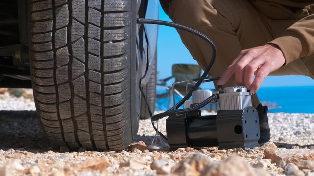 Man inflating a car tire with portable air compressor. Man's hands operating a portable air compressor to inflate a flat car tire during a road trip adventure, demonstrating vehicle maintenance