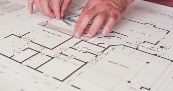 An architectural engineer takes measurements on a paper plan of a house using rulers and compasses.