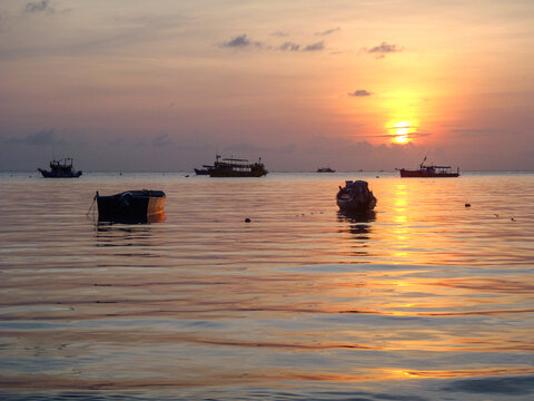Orange sunset over calm ocean with boats from beach on Ko Tao, Thailand