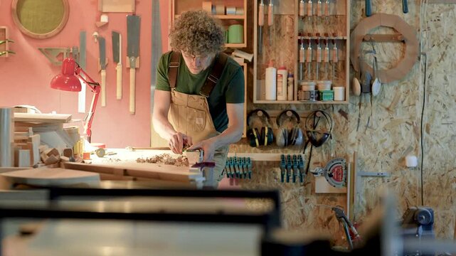 Working process in small wooden manufacture, carpenter creating new handmade furniture in workshop, carpentry business, design and creative project, man using hand plane and shaping wood board.