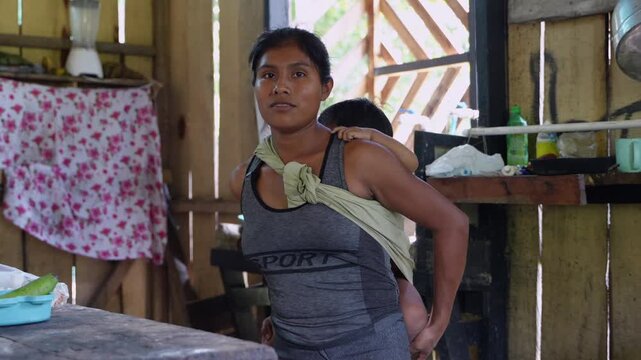 Indigenous mother carrying sleeping baby on back in a simple home