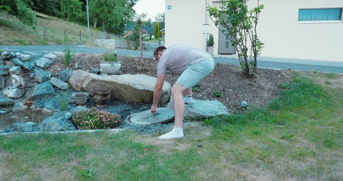 Man lifting a heavy manhole cover outdoors using physical force. Workplace safety concept of manual handling, back injury risk, improper lifting, and occupational hazards.
