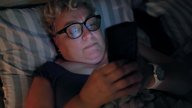 Overweight Mature Woman Browsing Social Media On Smartphone Lying In Bed At Night