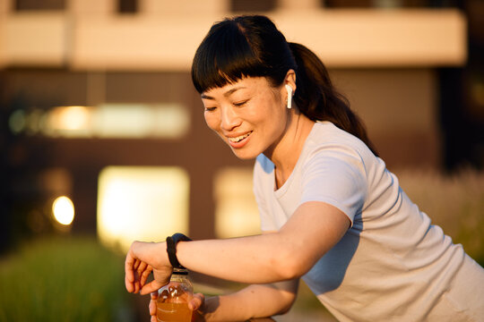 Portrait of a young beautiful sport woman smiling happy and confident. Standing and  doing exercise and stretching looking at watch and heart rate pulse  park outdoors