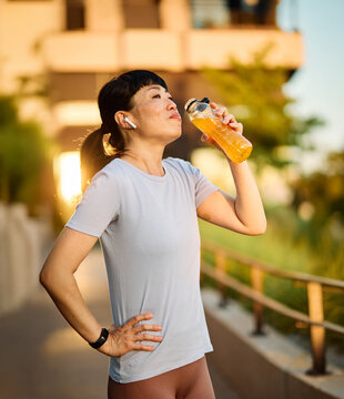 Portrait of a young beautiful sport woman smiling happy and confident. Standing and  doing exercise and stretching and holding a bottle of water or energy drink or juice during a break in city park ou