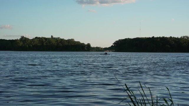 A man in a kayak sits calmly before gently beginning to paddle, creating a smooth transition from stillness to light motion. The scene conveys a sense of tranquility, outdoor leisure, active lifestyle