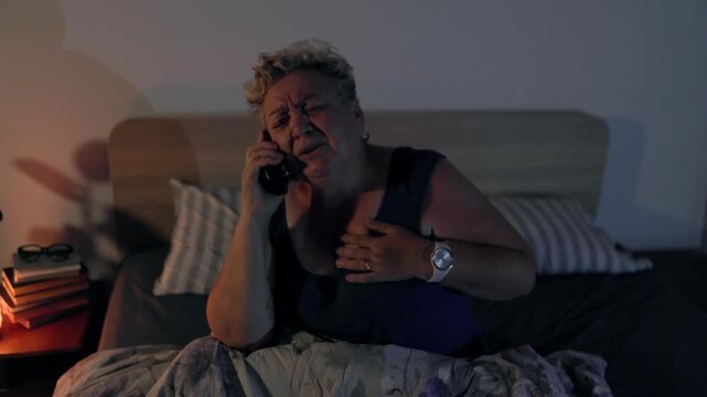 Overweight Senior Woman Clutching Chest Calling Ambulance In Bed At Night