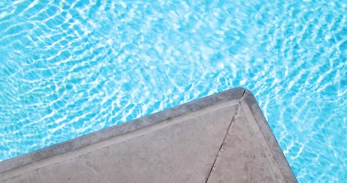 Slow motion footage of crystal clear blue swimming pool water with shimmering sunlight reflections surrounding a modern concrete pool corner creating a relaxing luxury holiday background