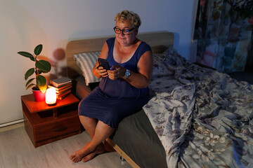 Obraz premium Senior female reading messages on smartphone in dimly illuminated bedroom.
