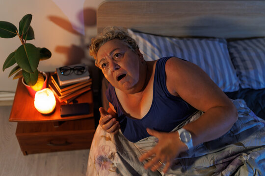 Overweight mature woman waking up from scary nightmare in dark bedroom.