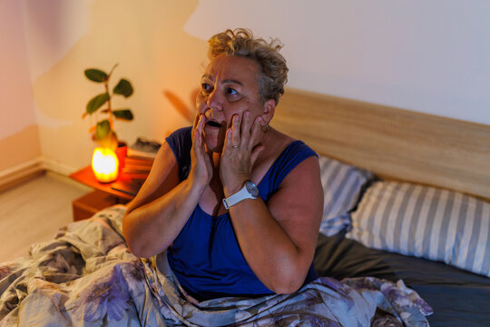 Scared overweight senior lady experiencing severe nightmare in dark room.