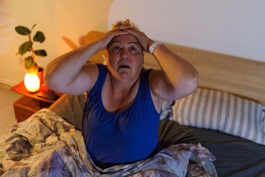 Overweight older woman experiencing nightmare touching head in bedroom.