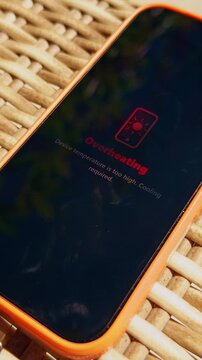 Vertical video. Smartphone With Overheating Warning Resting On Wicker Surface In Direct Sunlight, Mobile Technology And Summer Conditions