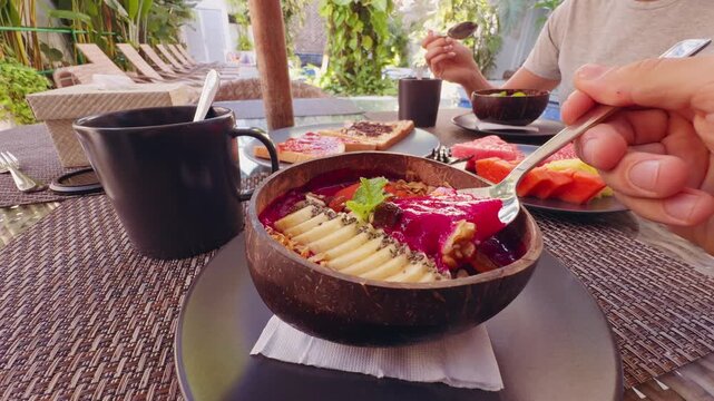 People Enjoying Tropical Breakfast With Smoothie Bowl Fresh Fruit Toast And Coffee at Poolside Resort Restaurant