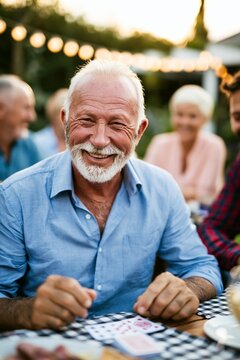 Cheerful senior man playing cards with family members at garden party
