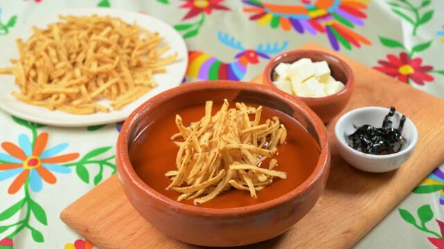 Hand adding crispy tortilla strips into traditional Mexican tortilla soup