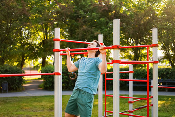 Obraz premium man doing a pullup exercise on a bar during an outdoor workout in a sunny park. Sport, fitness and strength training for a healthy lifestyle.