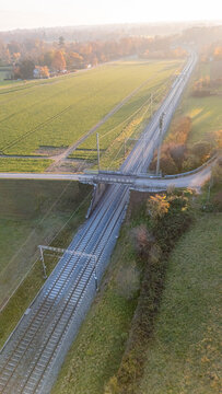 Aerial view of railway tracks passing under a road bridge through rural fields in Crans, Vaud, Switzerland.