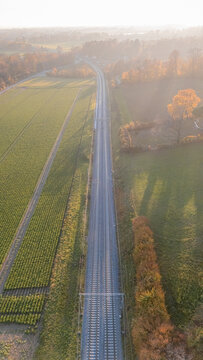 Aerial view of railway tracks stretching through rural fields and autumn trees in Crans, Vaud, Switzerland.
