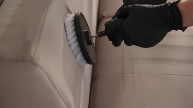 Dry wash procedure on a beige fabric sofa captured in 4K. Professional cleaner uses a power drill attachment to agitate upholstery stains