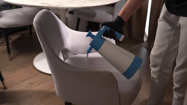 Chemical detergent spray application on a fabric dining chair captured in 4K. Cleaning worker applies solvent to upholstery