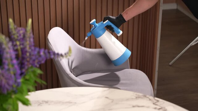 Upholstery sanitization spray on a dining chair surface in 4K. Cleaning worker agitates the fabric before moisture removal