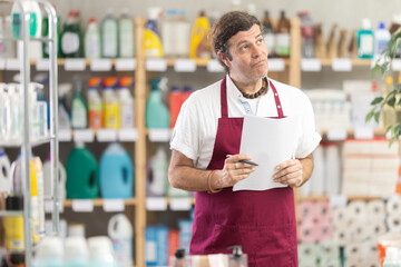 Obraz premium Anxious adult man seller with checklist in household chemicals store decorated for christmas