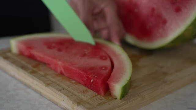 Meticulous process of preparing fresh watermelon. The footage highlights the detailed action of slicing away the green rind from the vibrant red flesh using a knife on a wooden cutting board. Tutorial