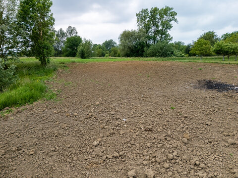 Barren agricultural field prepared for planting, surrounded by lush greenery and trees under overcast sky, illustrating rural farming and sustainable agriculture concepts.