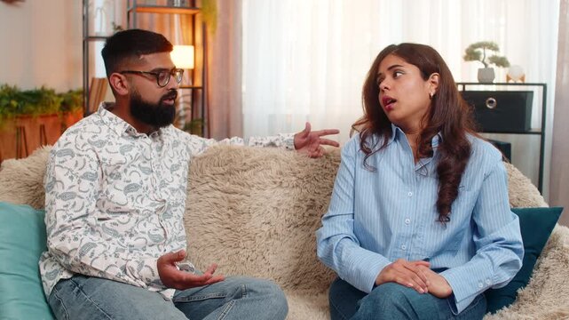 Indian couple man and woman sitting on home sofa, smiling and hugging after emotional moment of reconciliation and peace. Young family enjoying closeness, mutual support and restored harmony indoors
