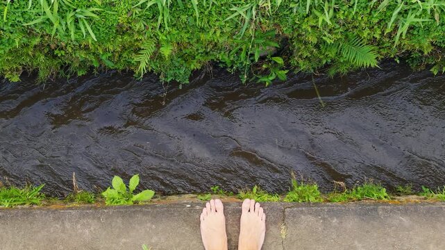Bare Feet Standing Above Fast Flowing Canal Water Viewed From Above