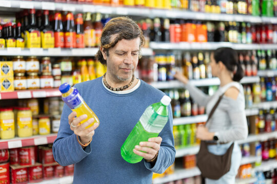 Man buyer examines assortment, reads product label information before buy drink. Client compares different options item, chooses product goods and check shelf life