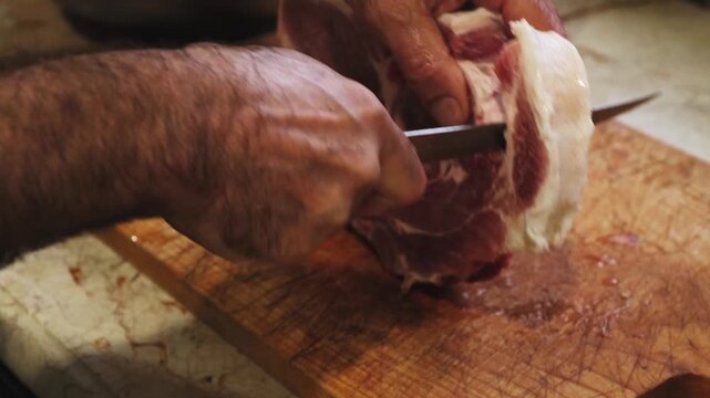 Close-up of a chef cutting fresh pork with a sharp knife on a wooden cutting board during barbecue preparation. Traditional cooking process using quality meat and authentic techniques.